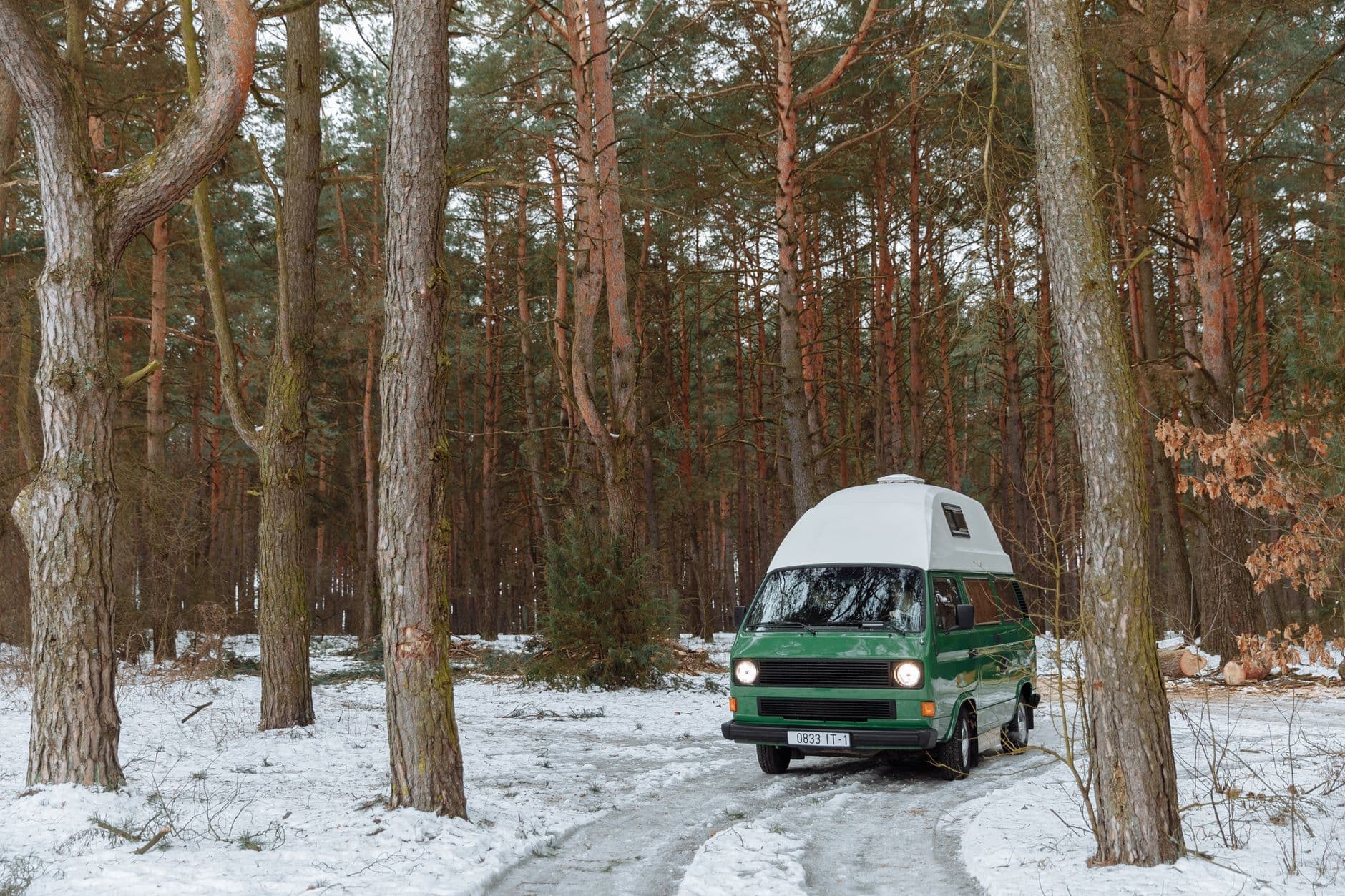 Vintage campervan parked in a snowy forest, encapsulating a serene winter camping vibe.