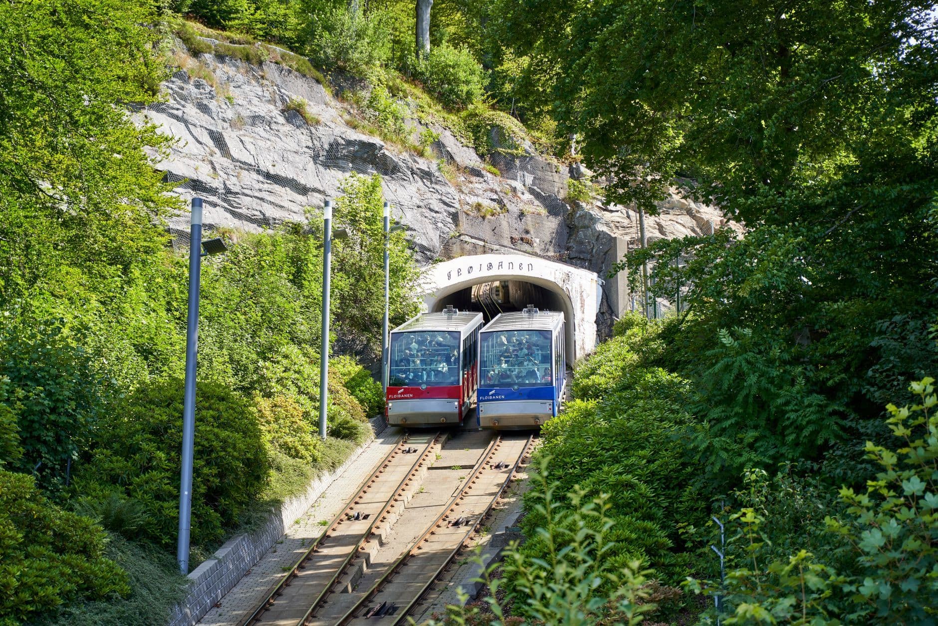 Double funiculars emerging from a tunnel in a lush green setting, Fløibanen, Bergen, Norway.