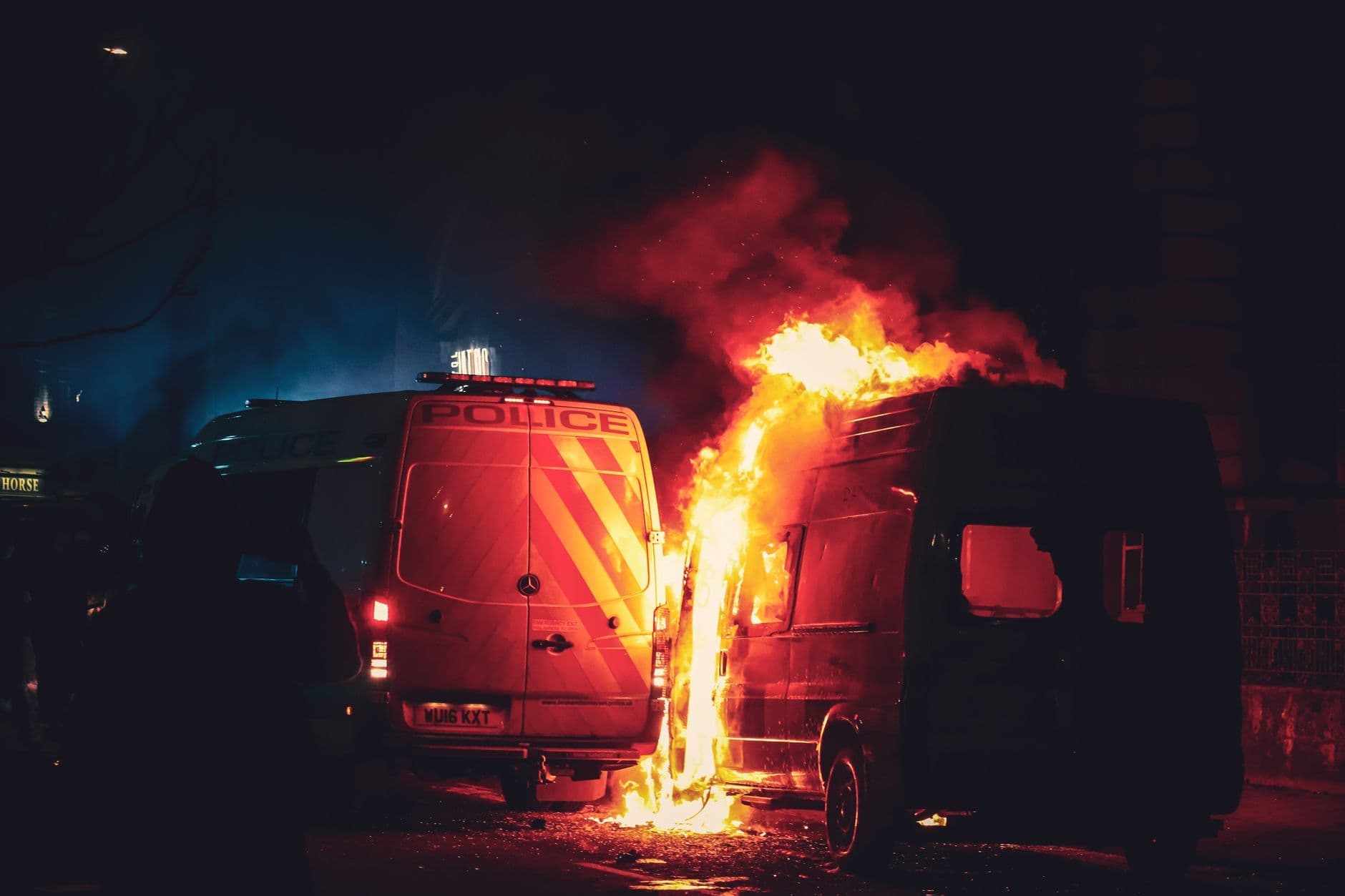 Intense night scene of a van on fire near police vehicles in Bristol, England.