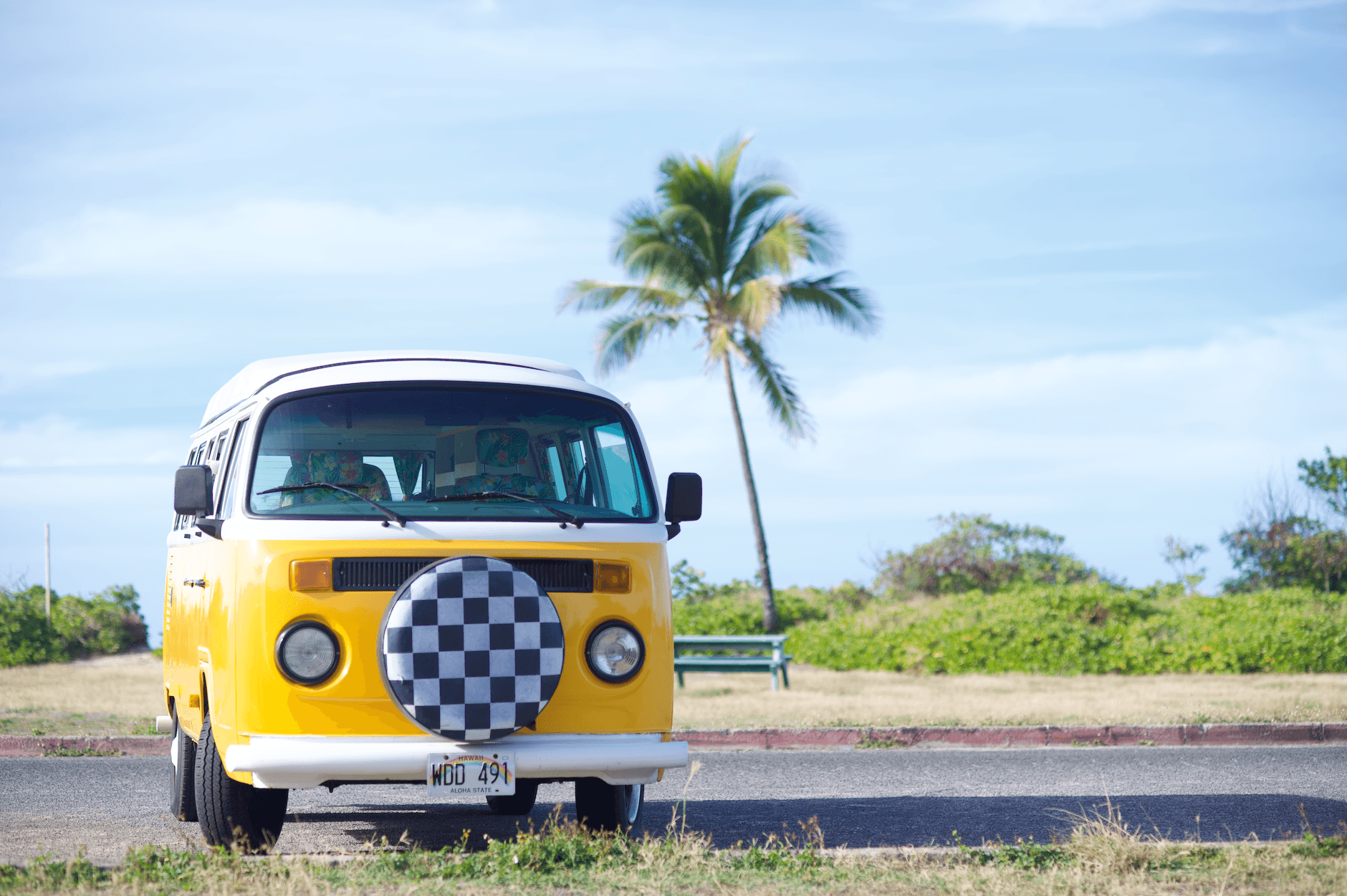 Classic yellow Volkswagen bus parked on a sunny Hawaiian day with a palm tree in the background.