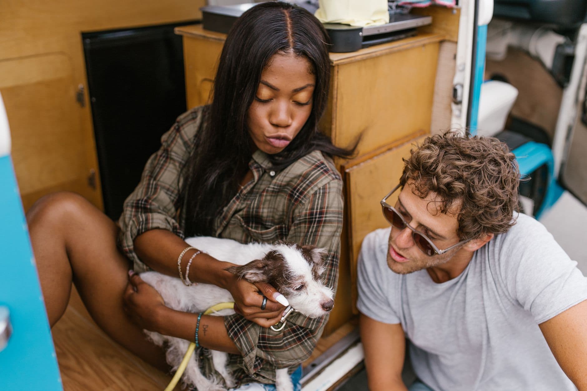 A young couple sits inside a campervan, lovingly interacting with their pet dog during a travel adventure.