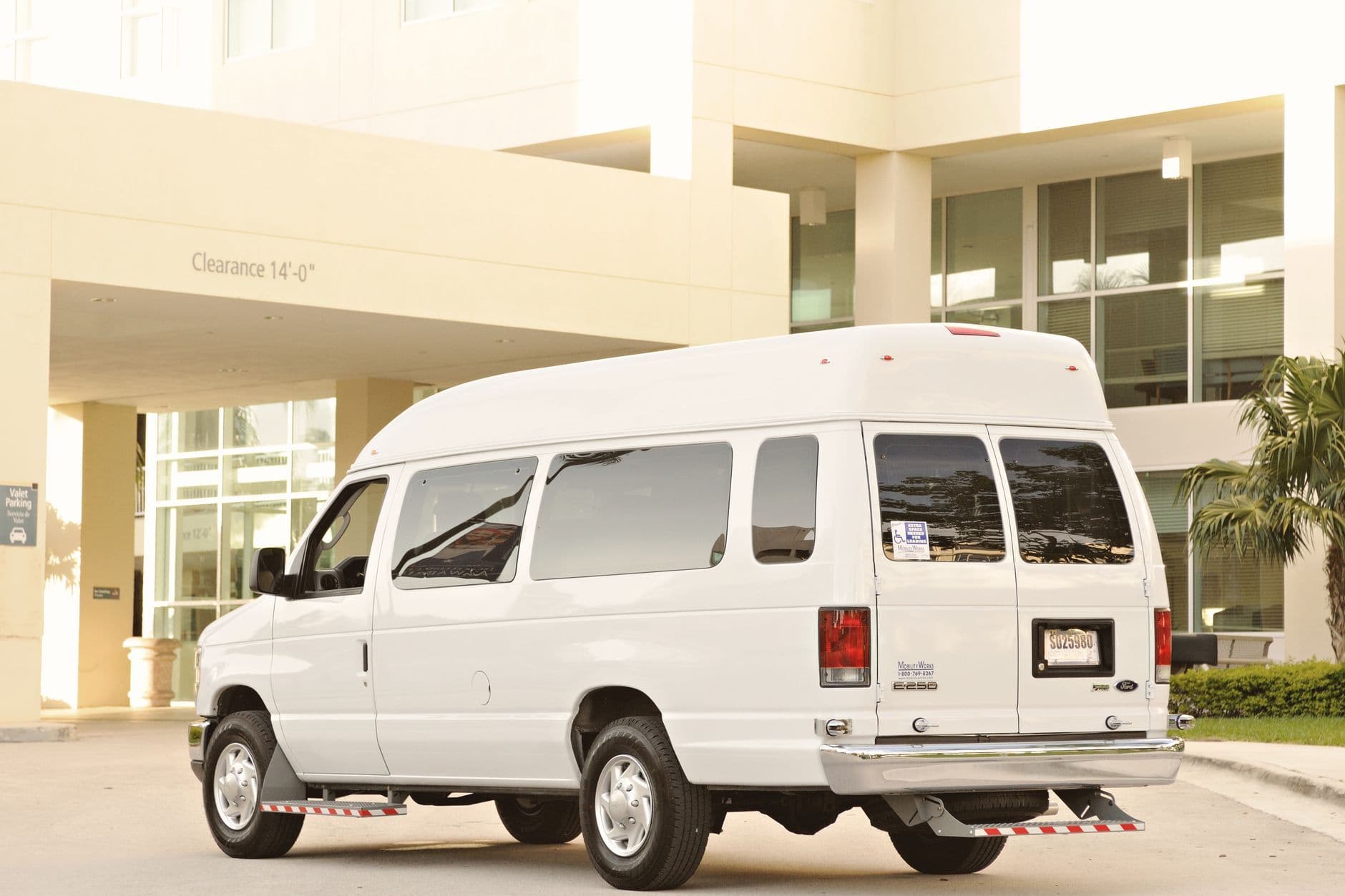 White passenger van parked outside a modern building under a clearance sign.