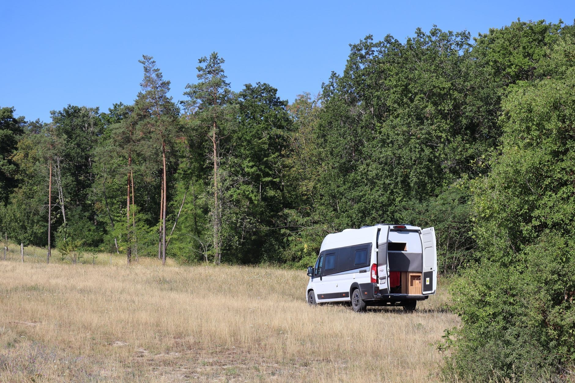White campervan parked in a grassy area near a forest in Fralignes, Grand Est, France.