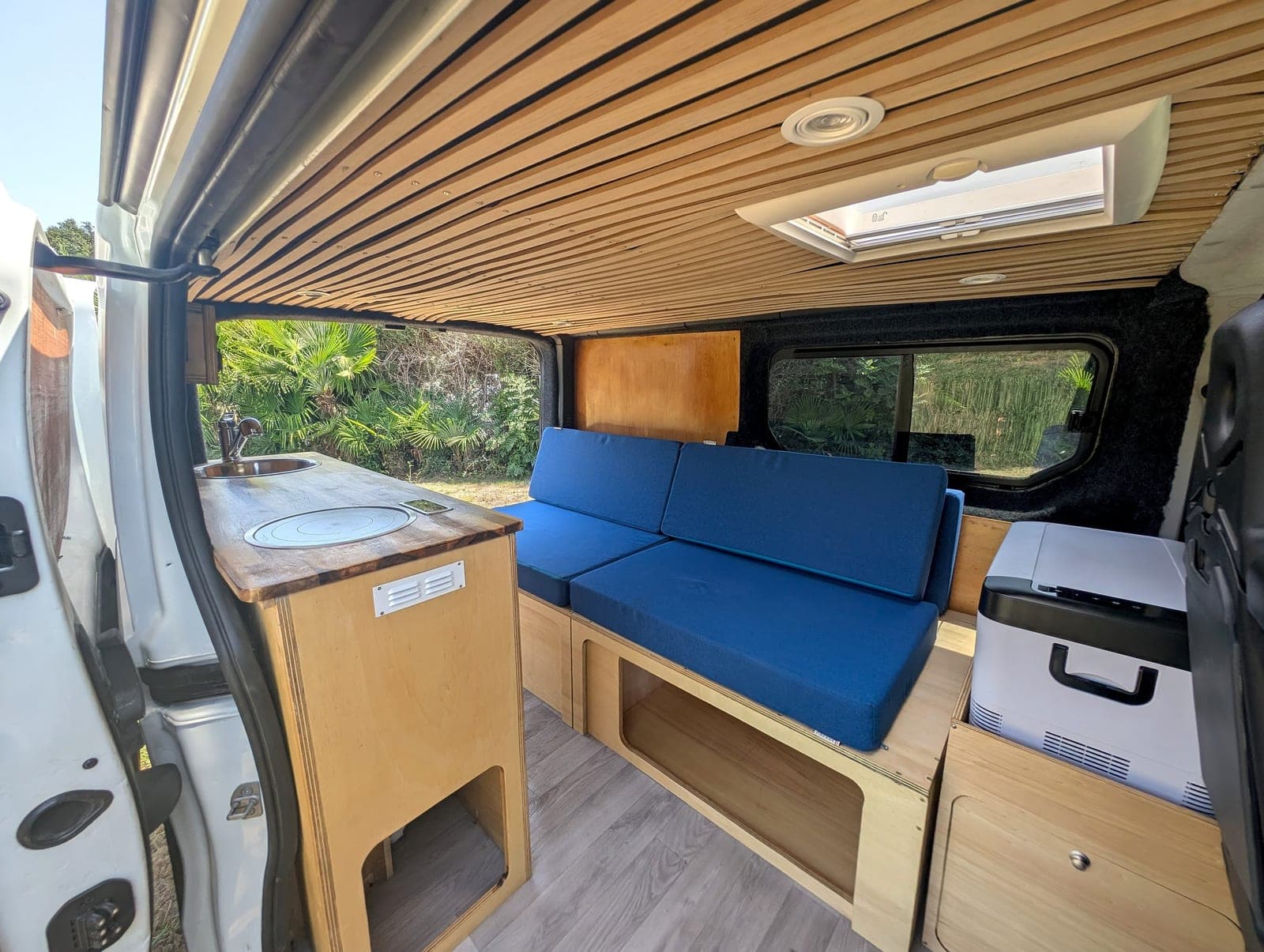 Salon avec banquette et coin cuisine d'un van aménagé Vanzon Explorer, porte latérale ouverte