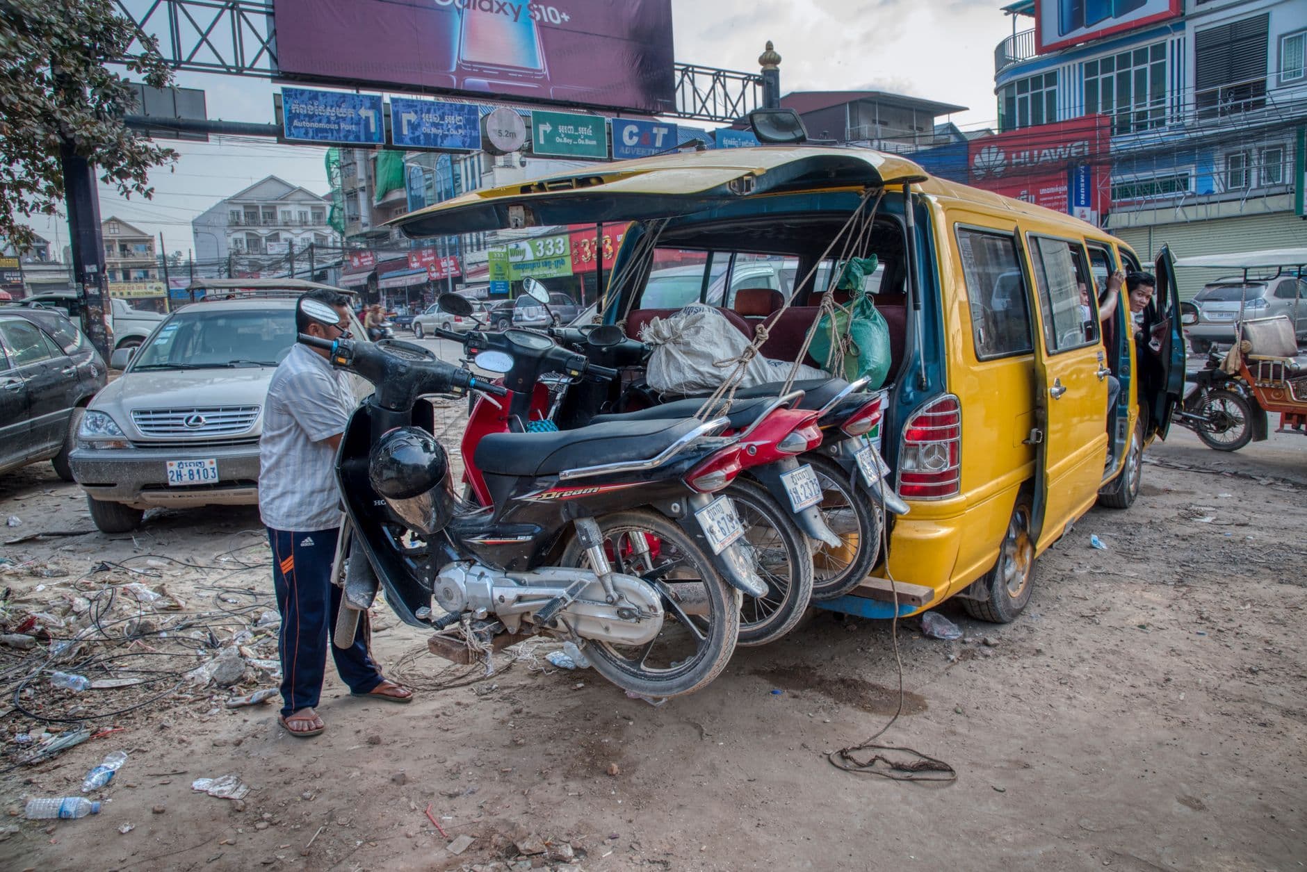 Motorcycles being loaded onto a van in a busy urban street scene, capturing the essence of daily transport.